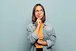 A contemplative woman wearing glasses and a denim jacket, thinking and looking away